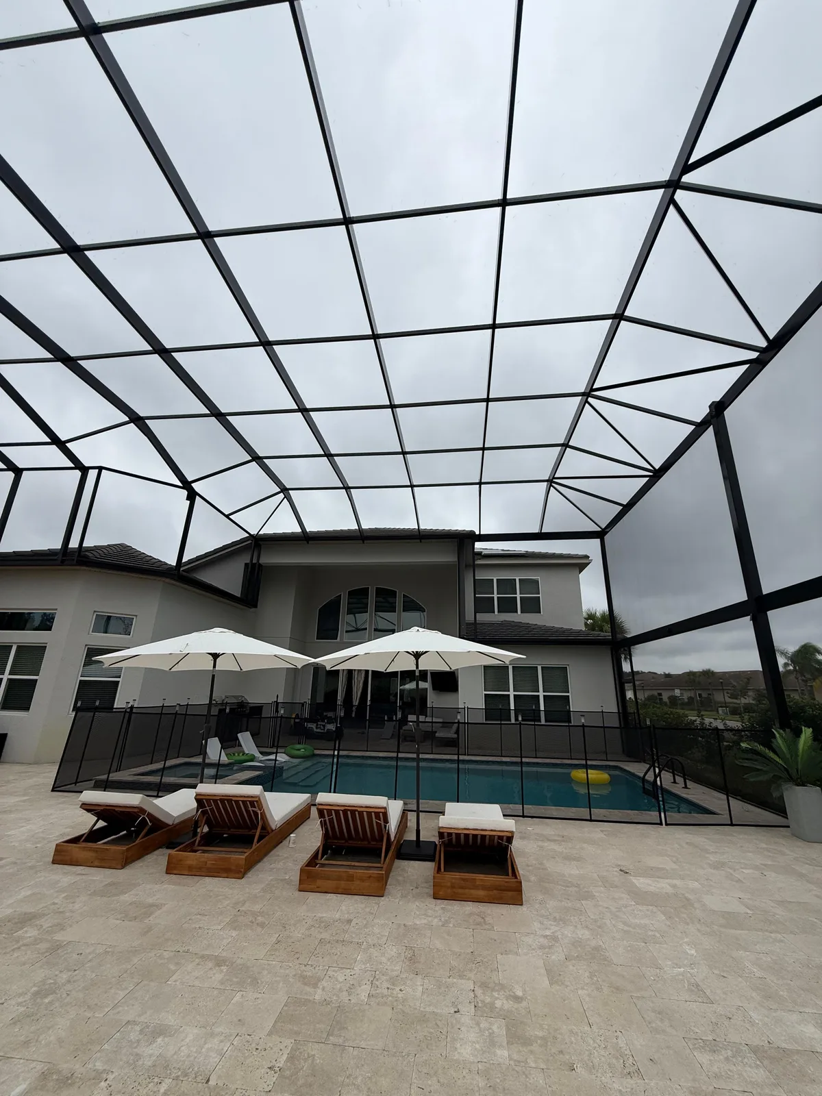 Interior view looking up at custom aluminum pool cage frame with pool, lounge chairs and umbrellas below, Florida