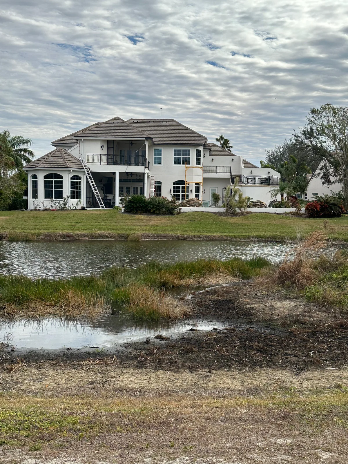 Before — large waterfront Florida home during screen enclosure installation, ladders and crew visible