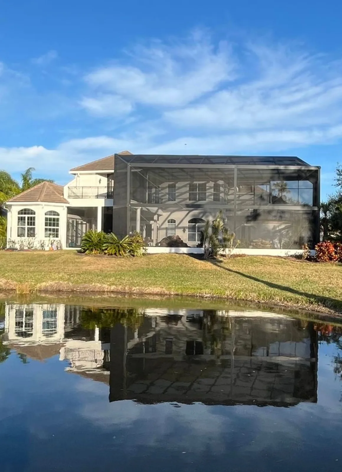 After — same luxury waterfront home with stunning completed screen enclosure and pond reflection, Southwest Florida