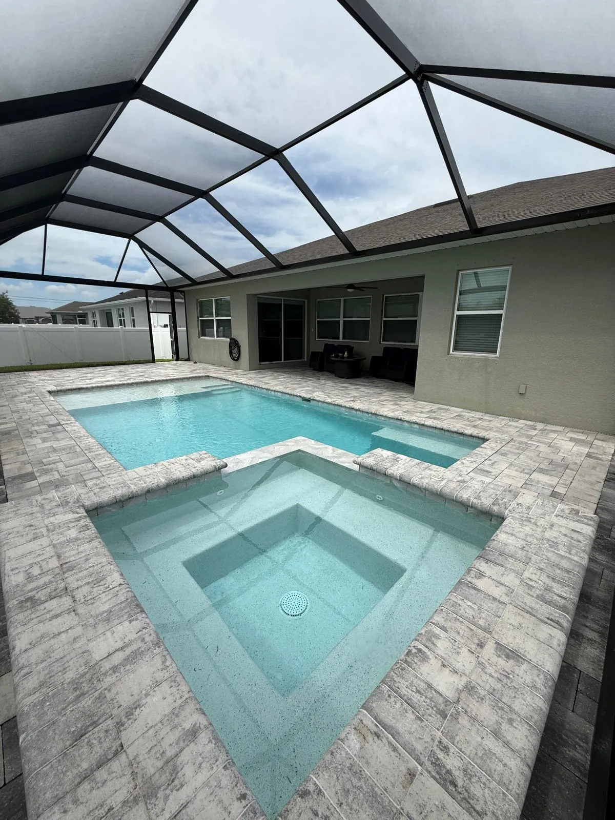 Aluminum pool cage enclosing pool and spa with travertine paver deck in Cape Coral, Florida