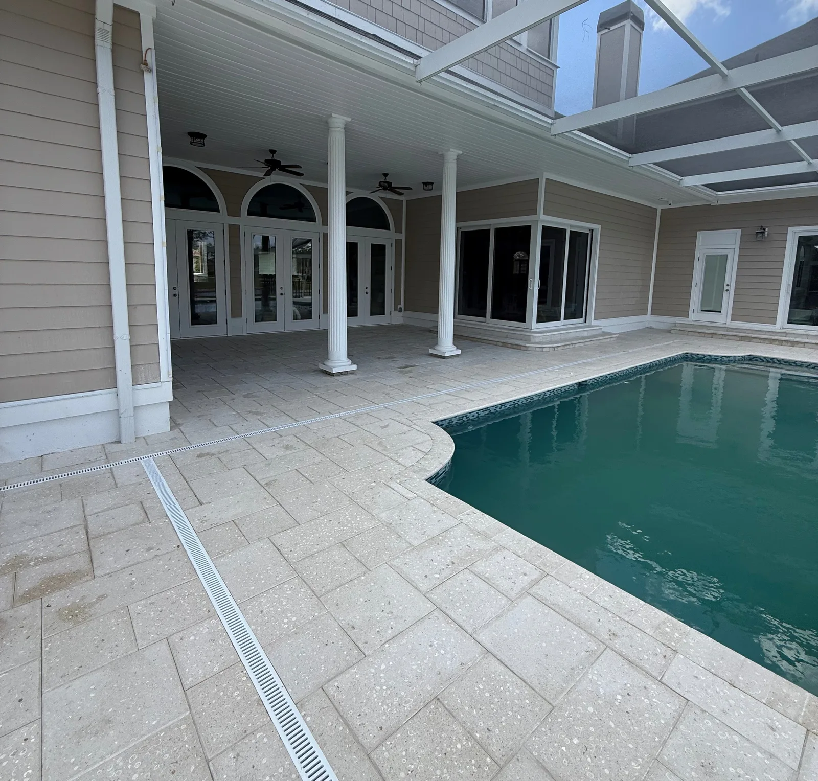 Travertine paver pool deck with covered patio, white columns and pool in Florida